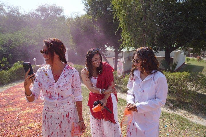 Three travellers in white kurtas splashed with red Holi colour in a garden