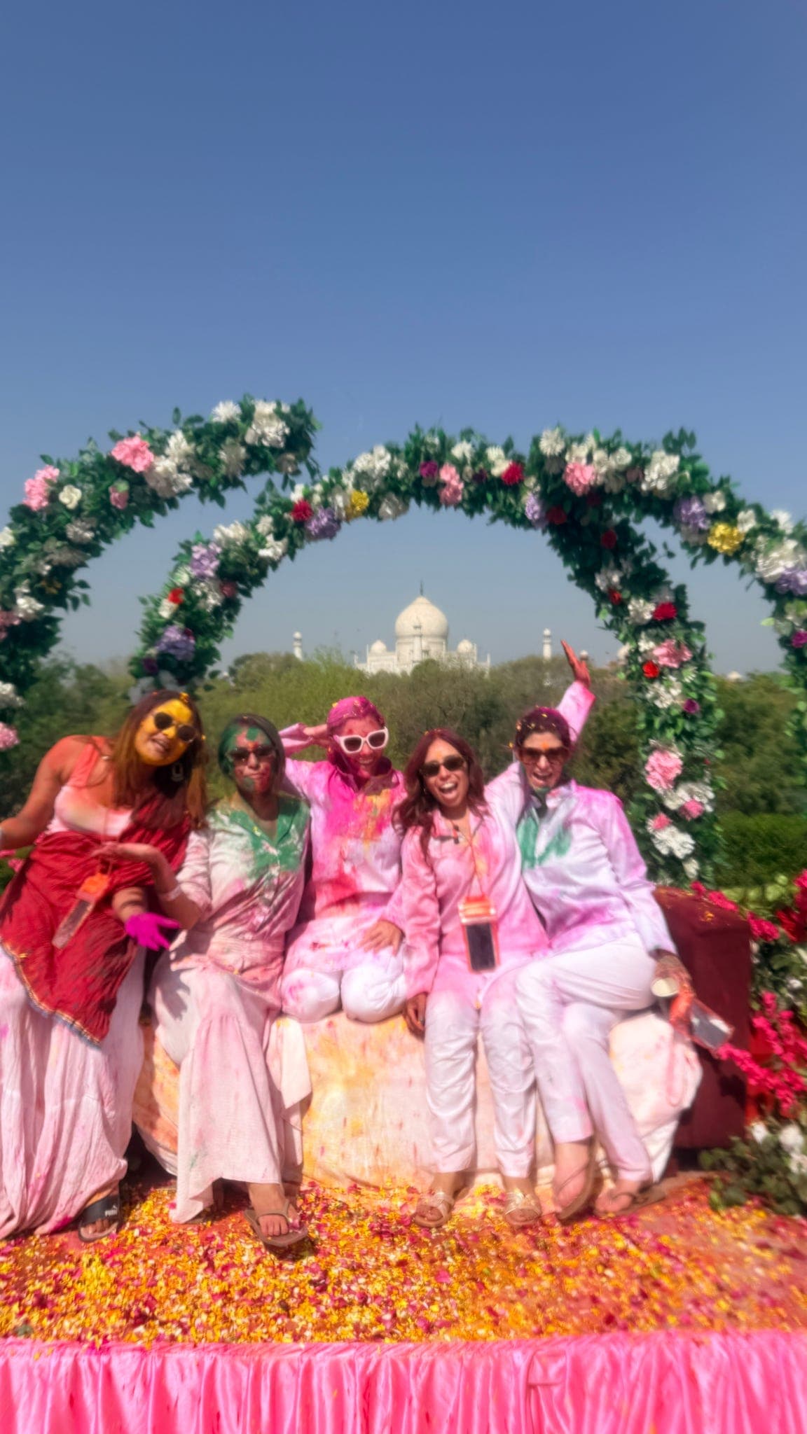 Travellers cheering in pink and green Holi colour among scattered flower petals