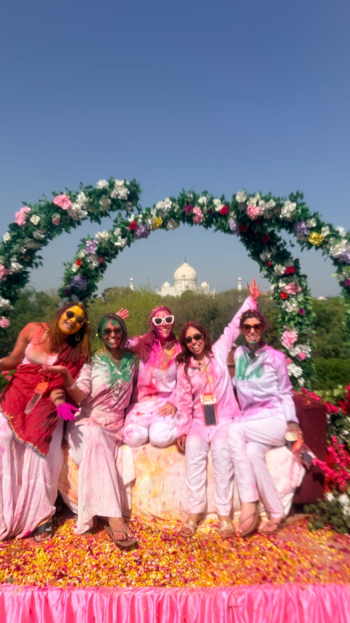 The Chalo Folks group posing in Holi colours under a flower arch in Agra