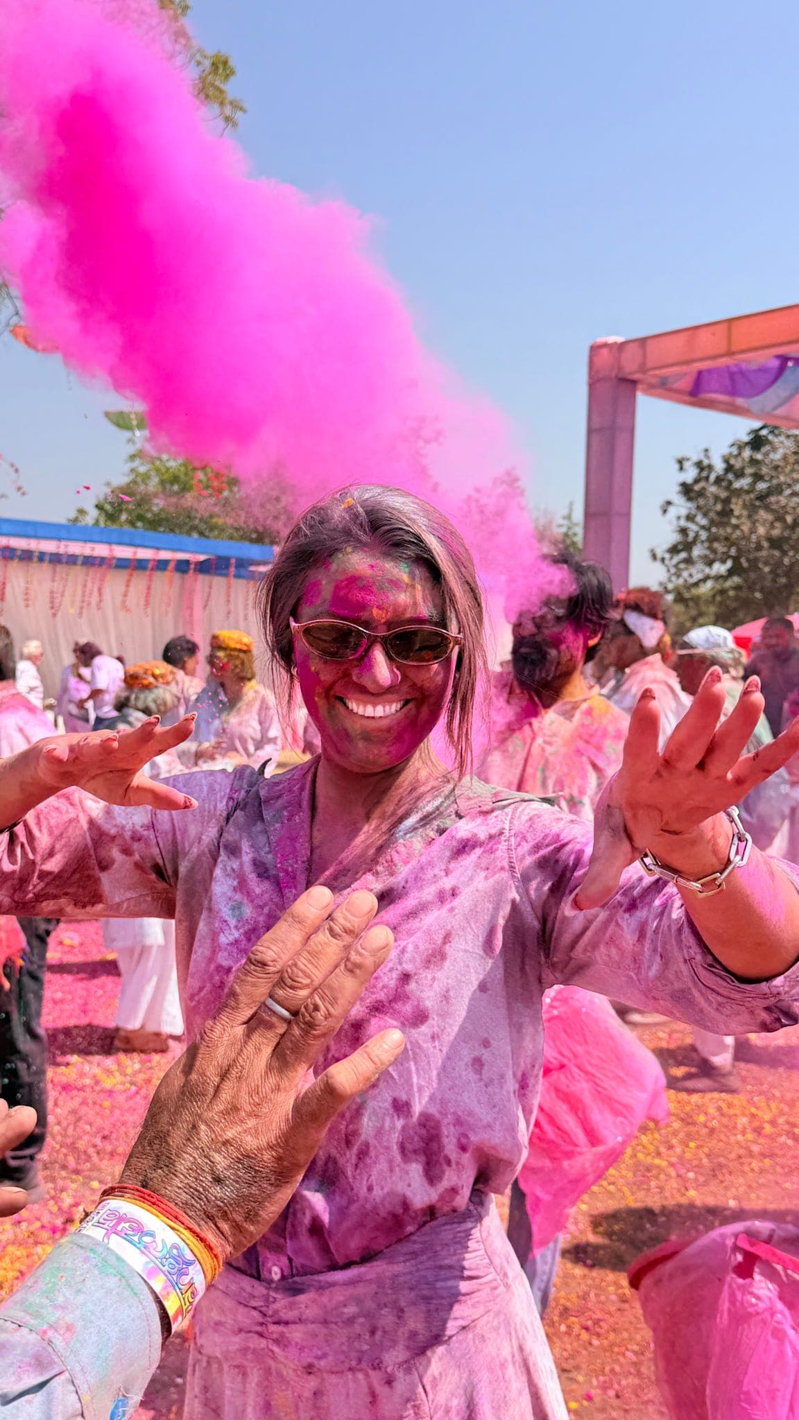 A traveller laughing as a cloud of pink gulal bursts overhead at the Holi celebration