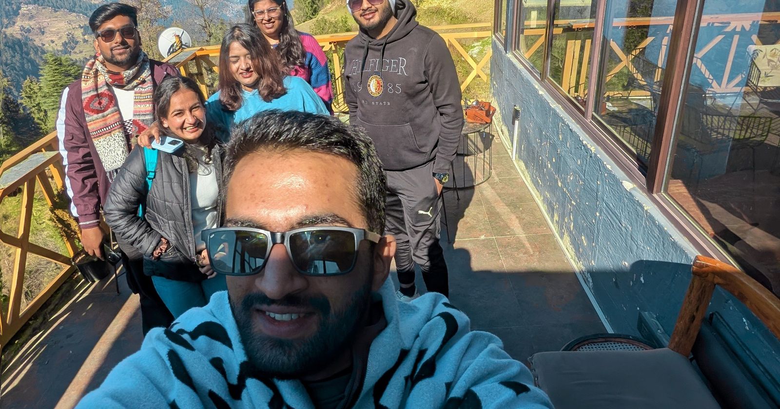 A small group of travellers taking a selfie on a sunny wooden balcony in the Himachal hills