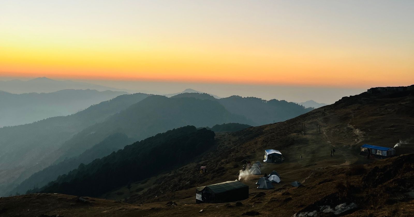 Sunset over layered Himalayan ridges above Jibhi, with tents on the slope below